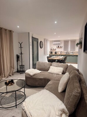 A modern living room with a sectional sofa, a glass coffee table, and a dining area in the background. - Spacious house near the lake - 6 people (Saint-Épain)