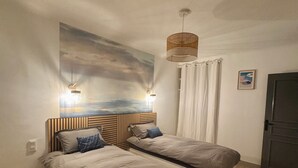 A bedroom with two beds, a wall-mounted artwork, a small round table, and a door. - Spacious house near the lake - 6 people (Saint-Épain)