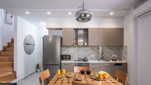 A modern kitchen with a wooden dining table set for breakfast, a clock on the wall, and a staircase on the left. - Iris Villa 3 (Archanes-Asterousia)