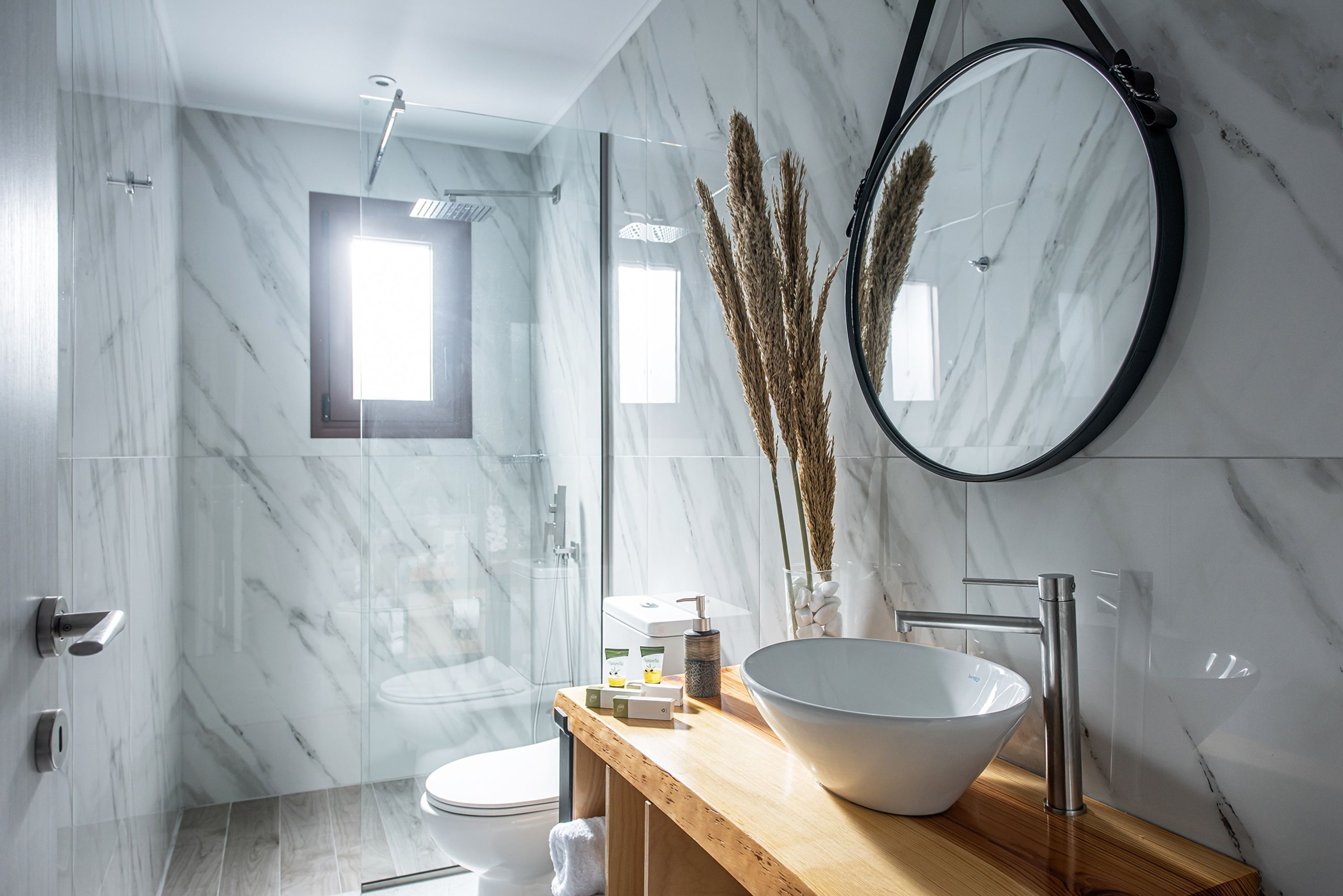Un baño moderno con un espejo grande, un tocador de madera, un lavabo blanco y un box de ducha de vidrio.