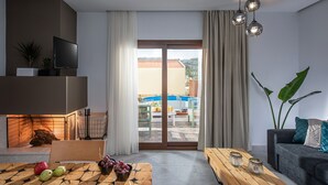 A modern living room with a television, wooden coffee table, and a view of a swimming pool and building outside. - Iris Villa 3 (Archanes-Asterousia)