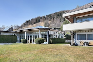 A modern house with a conservatory, a well-maintained lawn, and a view of a forested hill. - Room 'Bb Pattis 2P' with Mountain View, Balcony and Wi-Fi (Vipiteno)