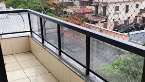 Ein Balkon mit Fliesenböden und Metallgeländer, der auf einen Wohnbereich mit Gebäuden und parkenden Autos blickt.