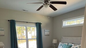 A bedroom with a bed, a ceiling fan, a window with curtains, and a nightstand with a lamp. - Relaxing 3-bedroom house close to
Holden Beach! (Supply)