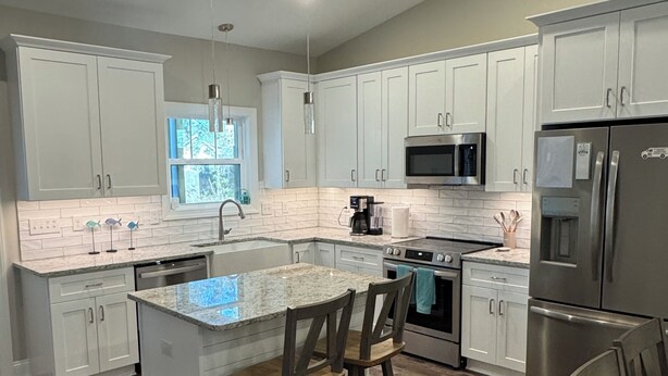 A modern kitchen with white cabinets, a granite countertop, stainless steel appliances, and a wooden island with bar stools. - Relaxing 3-bedroom house close to
Holden Beach! (Supply)