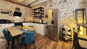 A kitchen with stone walls, a wooden dining table, blue chairs, a stainless steel refrigerator, and a hanging light fixture. - Holiday Home Tranquilla with heated pool (Blato)