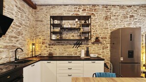 A kitchen with white cabinets, a stone wall, a built-in shelf with glassware, a stainless steel refrigerator, and a dining table with chairs. - Holiday Home Tranquilla with heated pool (Blato)