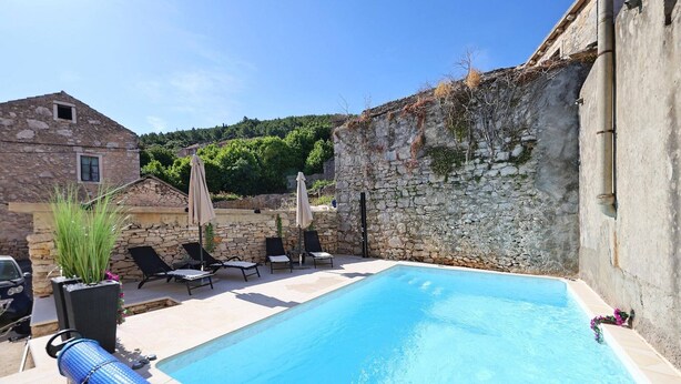 A swimming pool with lounge chairs and a stone wall. - Holiday Home Tranquilla with heated pool (Blato)