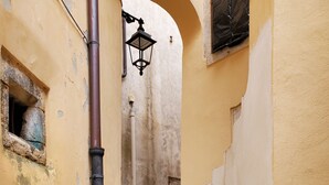 A narrow alleyway with stone steps leading to a doorway, flanked by buildings with peeling yellow paint and a black metal pole. - The little door. Your lake view home. (Barrea)