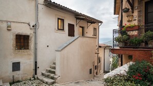 A narrow cobblestone street with a staircase leading to a building with multiple windows and a balcony with potted plants. - The little door. Your lake view home. (Barrea)