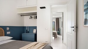 A modern bedroom with a bed, bedside table, wardrobe, and a view into another room. - The little door. Your lake view home. (Barrea)