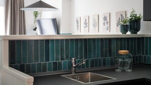 A modern kitchen with a dark green tiled backsplash, a stainless steel sink, and two potted plants on the counter. - The little door. Your lake view home. (Barrea)