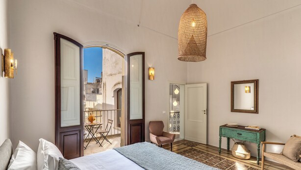 Una camera da letto con un letto, una sedia, un tavolino, uno specchio e vista sull'esterno.