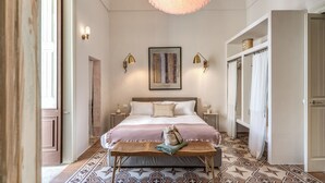 Camera da letto con un letto grande, comodini, una panca, un lampadario e un pavimento decorato.