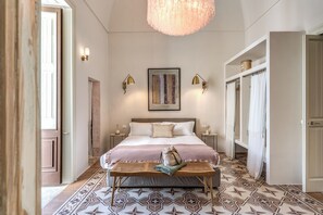 Camera da letto con un letto grande, comodini, una panca, un lampadario e un pavimento decorato.