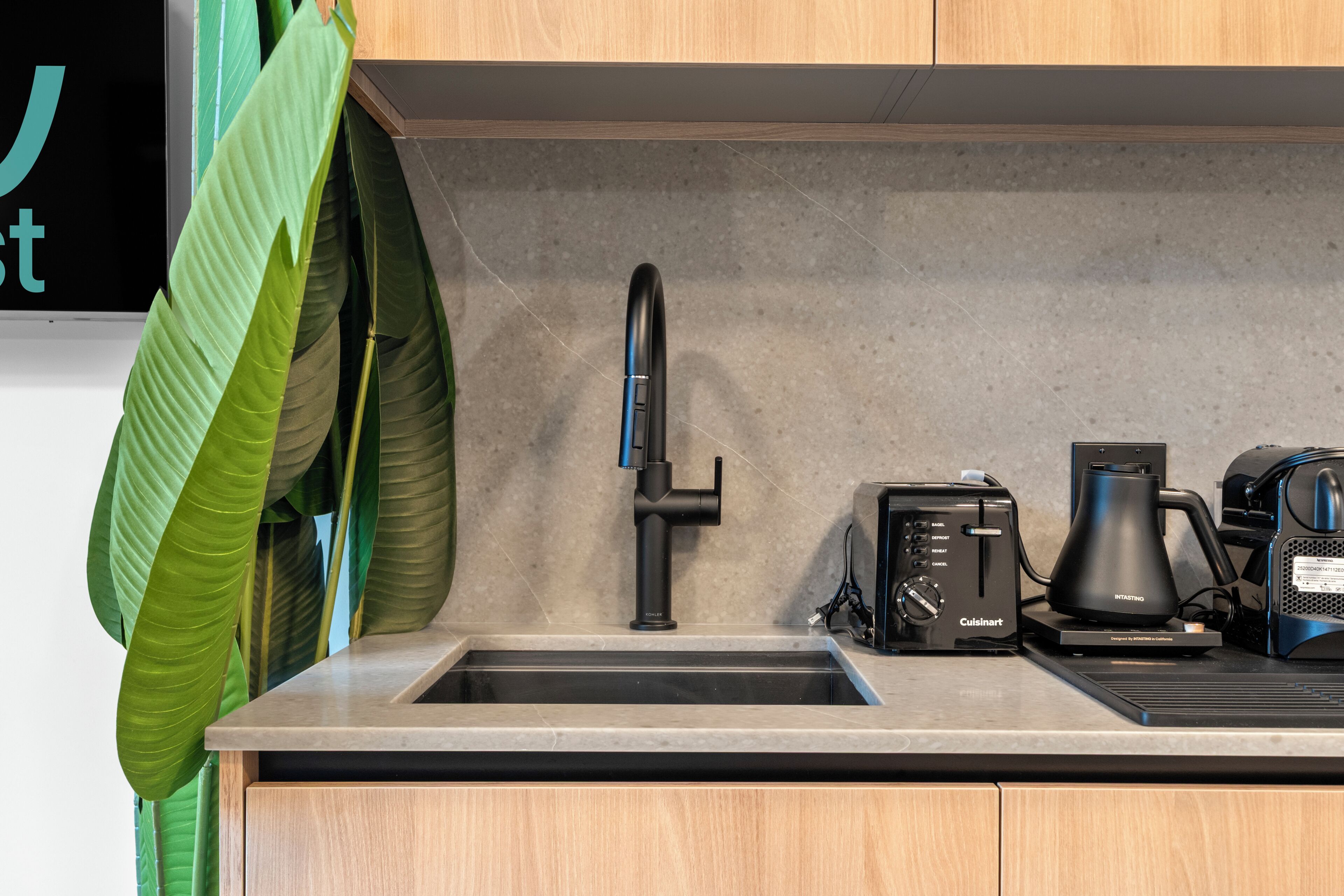 A modern kitchen with a black faucet, a Cuisinart toaster, and a coffee maker on the countertop.
