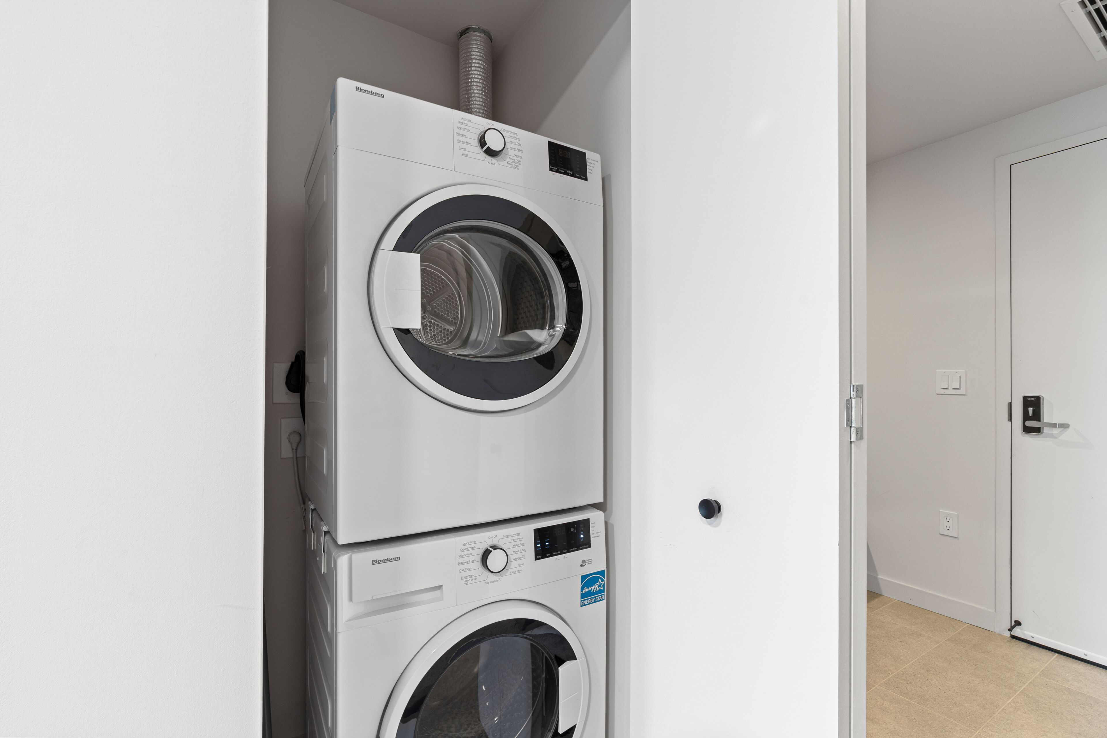 Lavadora y secadora apiladas en una habitación con una puerta blanca y paredes de tonos claros.