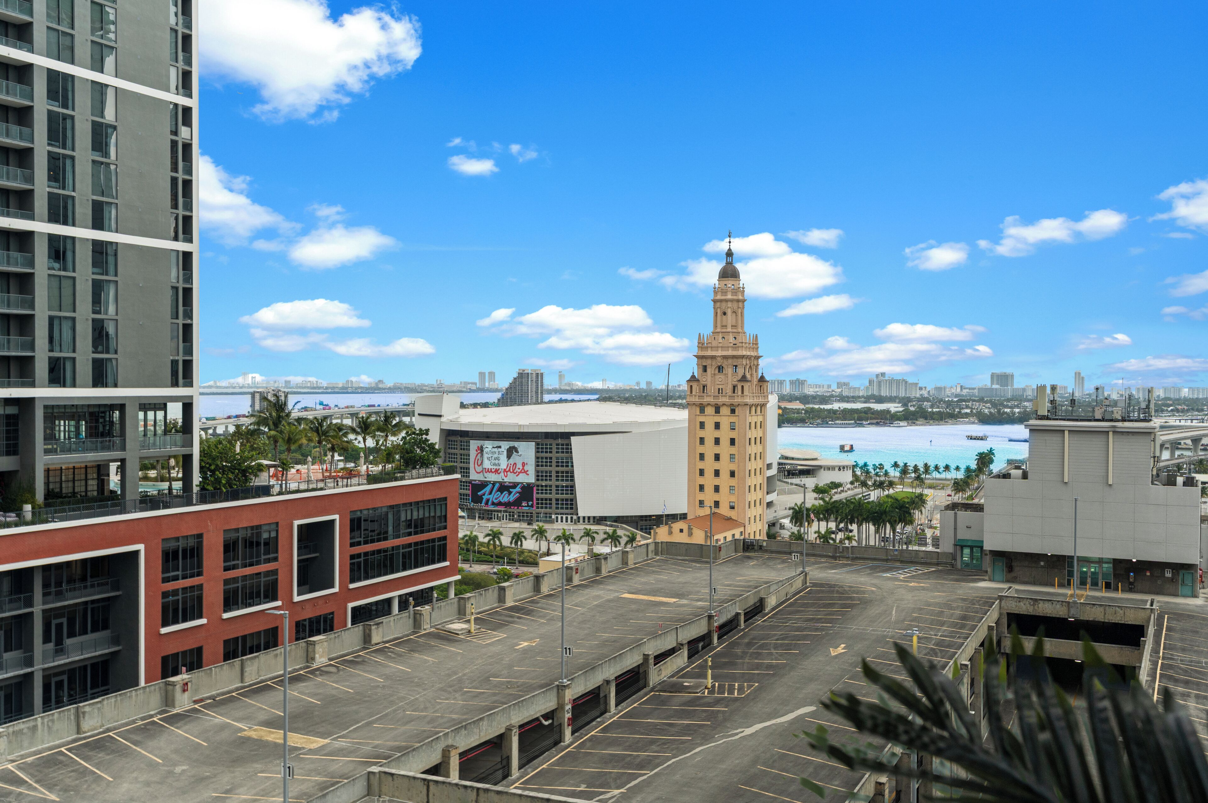 A parking lot with a view of a cityscape, including a tall building with a clock tower and a modern building with a large sign.