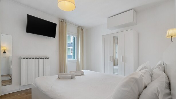 Une chambre d’hôtel moderne dotée d’un grand lit, d’un téléviseur à écran plat, d’un radiateur et d’une fenêtre avec des rideaux.