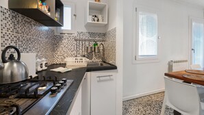 Une cuisine équipée d’une cuisinière à gaz, d’une bouilloire, d’un évier et de meubles de rangement blancs.