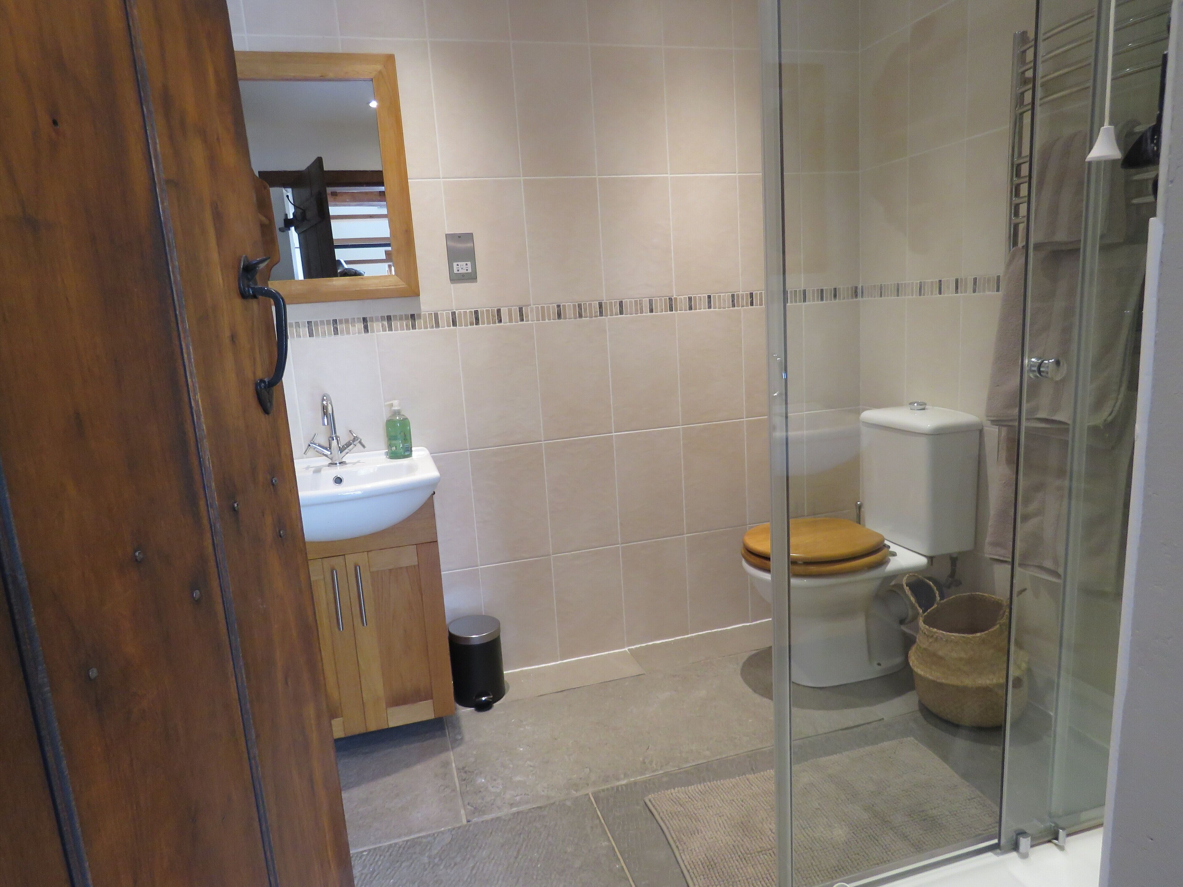 A bathroom with a wooden cabinet, a sink, a toilet, and a glass shower enclosure.