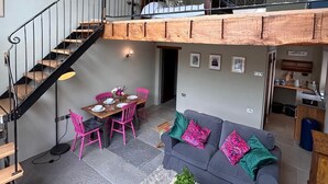 Un ambiente abitativo in stile loft con una scala, un'area pranzo, un divano e una piccola cucina.