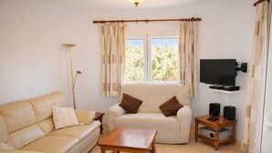 Ein Wohnzimmer mit Sofa, Sessel, Couchtisch, Fernseher, Lautsprechern und einer Lampe.