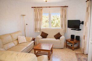 Ein Wohnzimmer mit Sofa, Sessel, Couchtisch, Fernseher, Lautsprechern und einer Lampe.