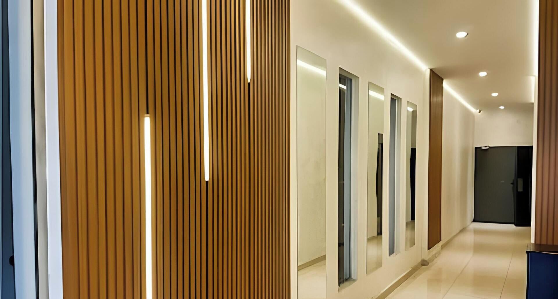 Un couloir moderne avec des lambris en bois verticaux, un éclairage encastré et des panneaux miroirs sur les murs.