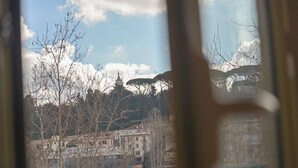 Une vue à travers une fenêtre, avec des arbres sans feuilles et des bâtiments en arrière-plan.
