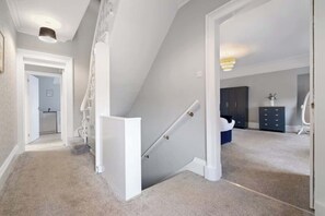 Eine Treppe führt zu einer zweiten Etage, ein Flur mit einer Tür und ein Zimmer mit Kommode und Schränken.