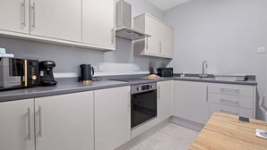 A modern kitchen with grey cabinets, a built-in oven, a coffee maker, and a sink. - Leo Apartment - 4 Bedroom Flat in Nairn (Nairn)