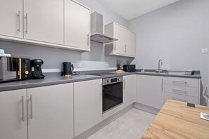 Eine moderne Küche mit grauen Schränken, einem Einbauofen, einer Kaffeemaschine und einem Spülbecken.