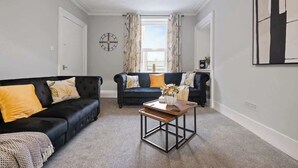 A living room with two dark sofas, a wooden coffee table, and a large abstract painting on the wall. - Leo Apartment - 4 Bedroom Flat in Nairn (Nairn)