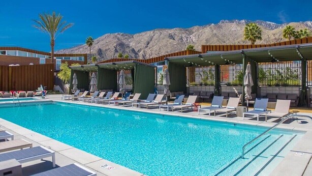 A pool area with lounge chairs and umbrellas, a clear blue pool, and a mountainous backdrop.