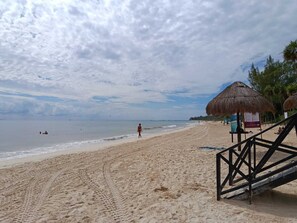 A beach with a thatched-roof structure, a sandy path, and a person walking. - Studio Sofia, a few steps from 88 Blue Flag Beach, (pets allowed). (Playa del Carmen)