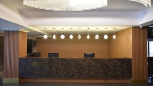 Vastaanottotiski, jonka päällä on marmorilevy ja jossa lukee sana ”RECEPTION”. Tiskin yläpuolella on useita riippuvalaisimia.