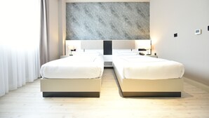 Moderni hotellihuone, jossa on kaksi sänkyä, suuri seinälle asennettu taideteos ja minimalistinen sisustus.