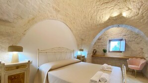 Ein Schlafzimmer mit Steinwand, einem Bett mit Kopfteil, einem Nachttisch mit Lampe, einem Sessel und einem Fenster mit Blick.