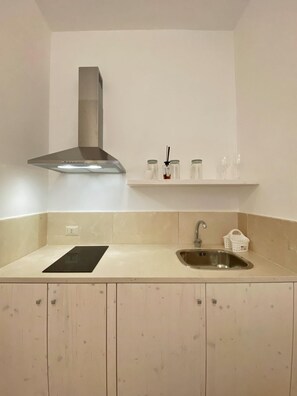 A compact kitchen with a stainless steel sink, a black induction cooktop, a stainless steel range hood, and a white countertop. - Trullo at the village (Puglia)