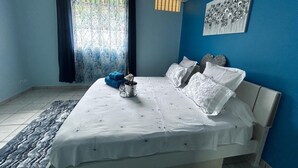 Un dormitorio con cama, ventana con cortinas, aire acondicionado de pared y una ventana pequeña con persianas.