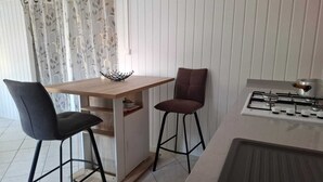 Pieni, käytännöllinen keittiö, jossa on puinen pöytä, kaksi baarituolia, kaasuliesi ja pesuallas.