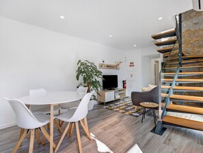 Un salon moderne comprenant un coin repas, un téléviseur, une plante et un escalier.