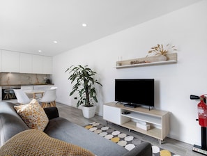 A modern living room with a sofa, a TV, a potted plant, a kitchen in the background, and a 'Welcome' sign on the wall. - Holiday Home 'Do Sol' with Shared Pool, Wi-Fi and Air Conditioning (Dornelas)