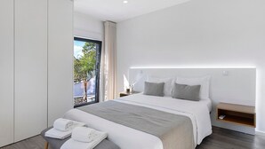 Una camera da letto moderna con un letto grande, un comodino, una panca con asciugamani e vista sull'esterno.