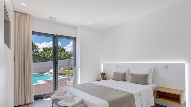 A modern bedroom with a bed, bedside table, and a view of an outdoor swimming pool. - Holiday Home 'Casa Da Oliveira' with Shared Pool, Wi-Fi and Air Conditioning (Dornelas)