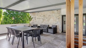 An outdoor patio with a stone wall, a dining table with chairs, and a seating area with sofas. - Holiday Home 'Casa Da Oliveira' with Shared Pool, Wi-Fi and Air Conditioning (Dornelas)