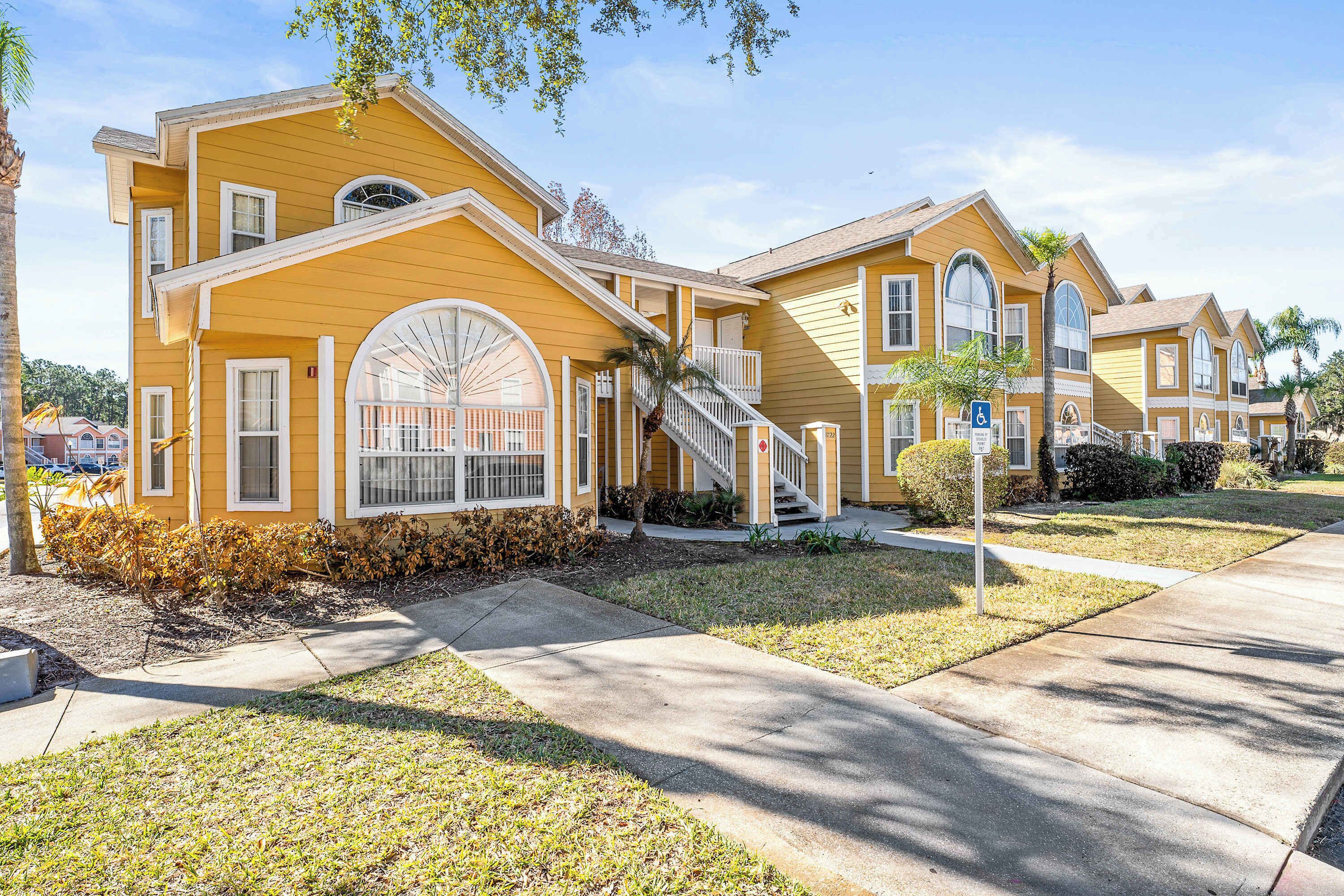 A yellow building with a staircase leading to the entrance, a wheelchair-accessible ramp, and a small garden area.