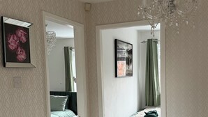 Une chambre à coucher comprenant un lit, une table de chevet, un lustre et une porte donnant sur une autre pièce.