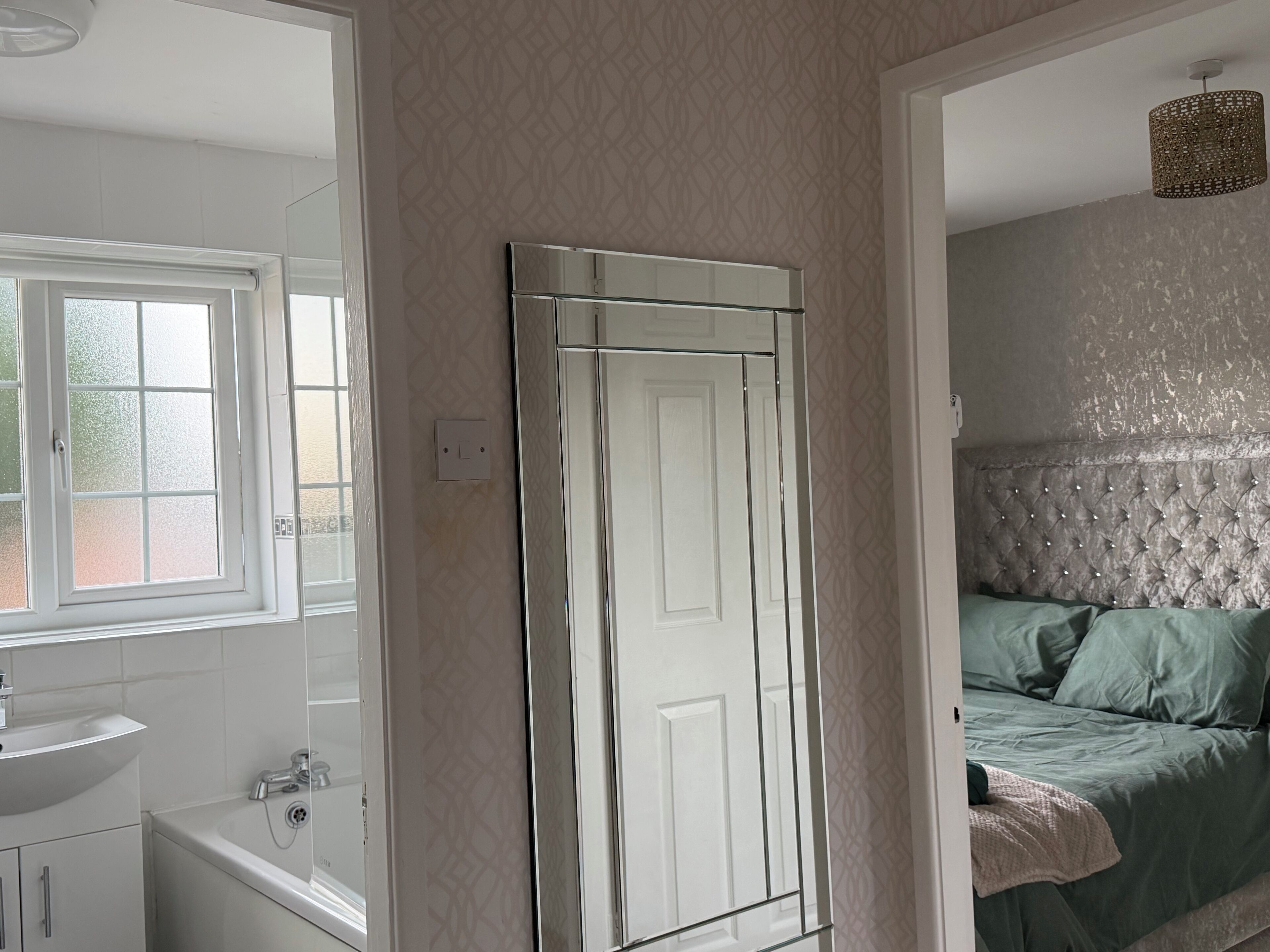A bedroom with a bed, a window, a bathroom with a sink, and a mirror.